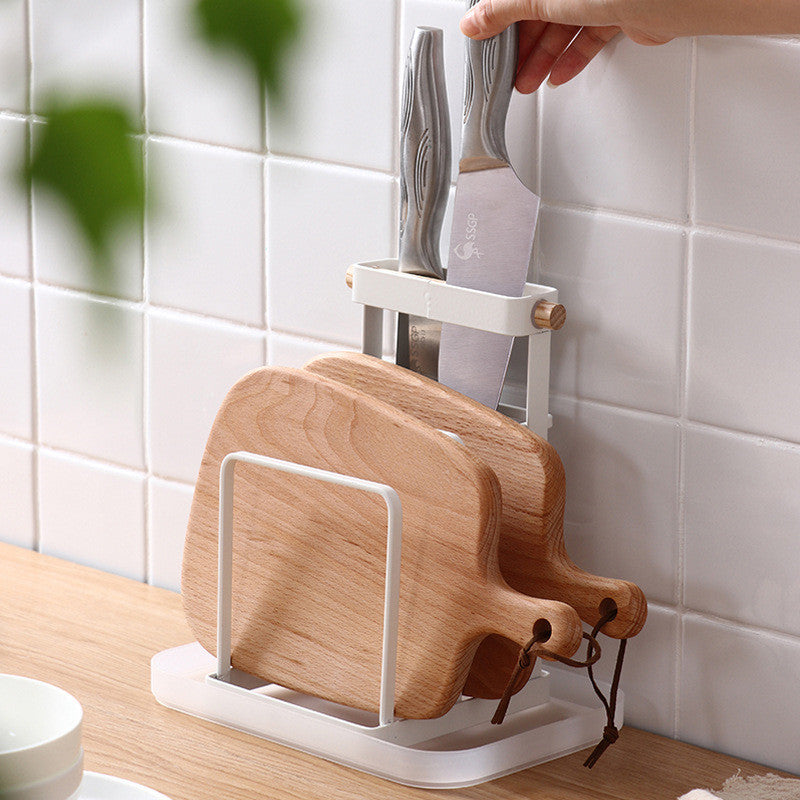 Black metal kitchen knife and cutting board rack holding knives and a wooden board on a countertop